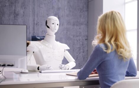 Robot Behind A Desk Conducting A Conversation With A Young Woman In Business Attire.